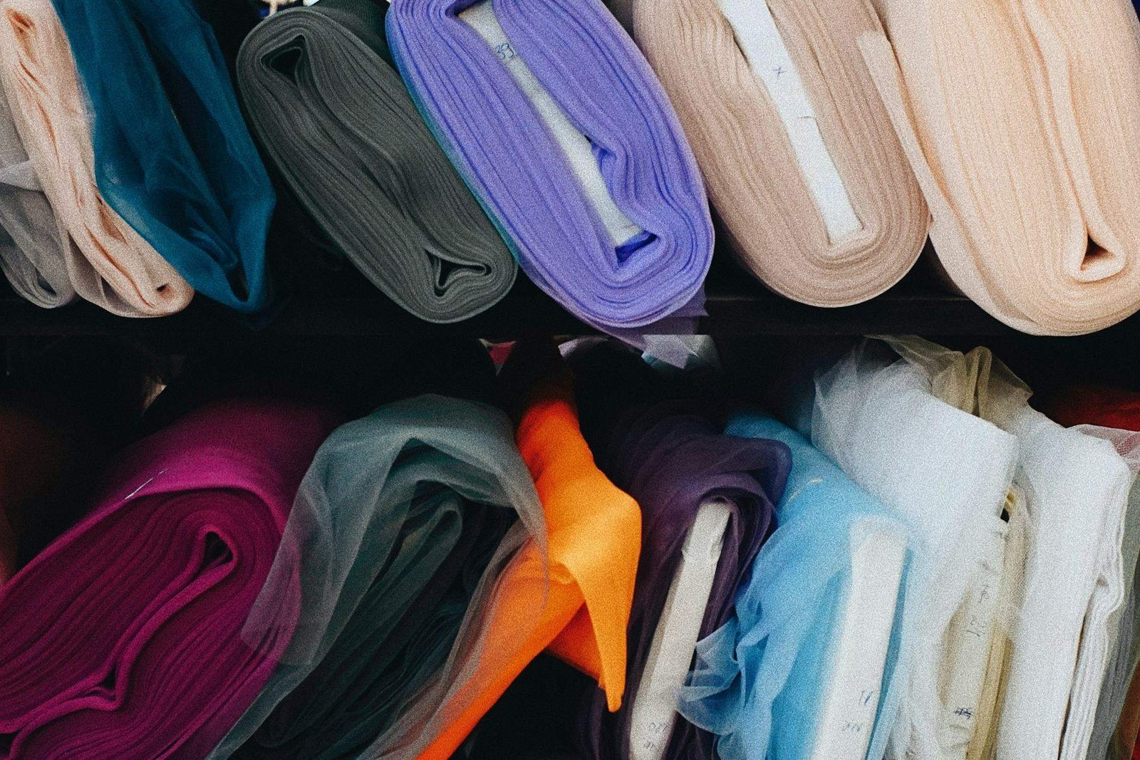 Rolls of fabric in many colours stacked on warehouse shelving